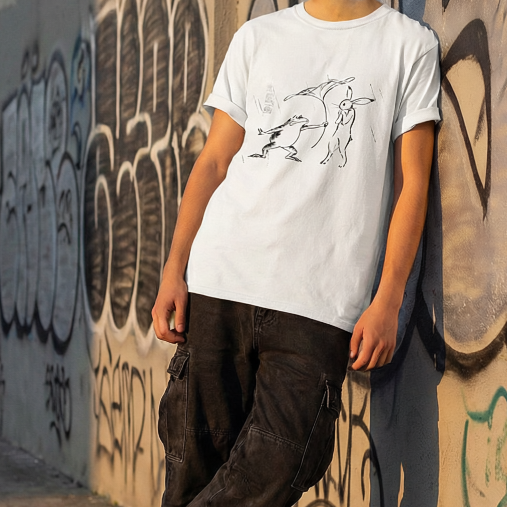 Person wearing a white t-shirt and dark pants leaning against a graffiti-covered wall.